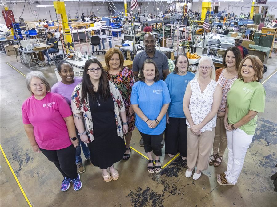 Members of the Alabama Industries for the Blind Customer Service Department smile to camera from the production room floor.